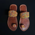 Pair of brown sandals with colorful beaded straps on a black background