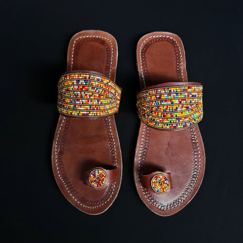 Pair of brown sandals with colorful beaded straps on a black background