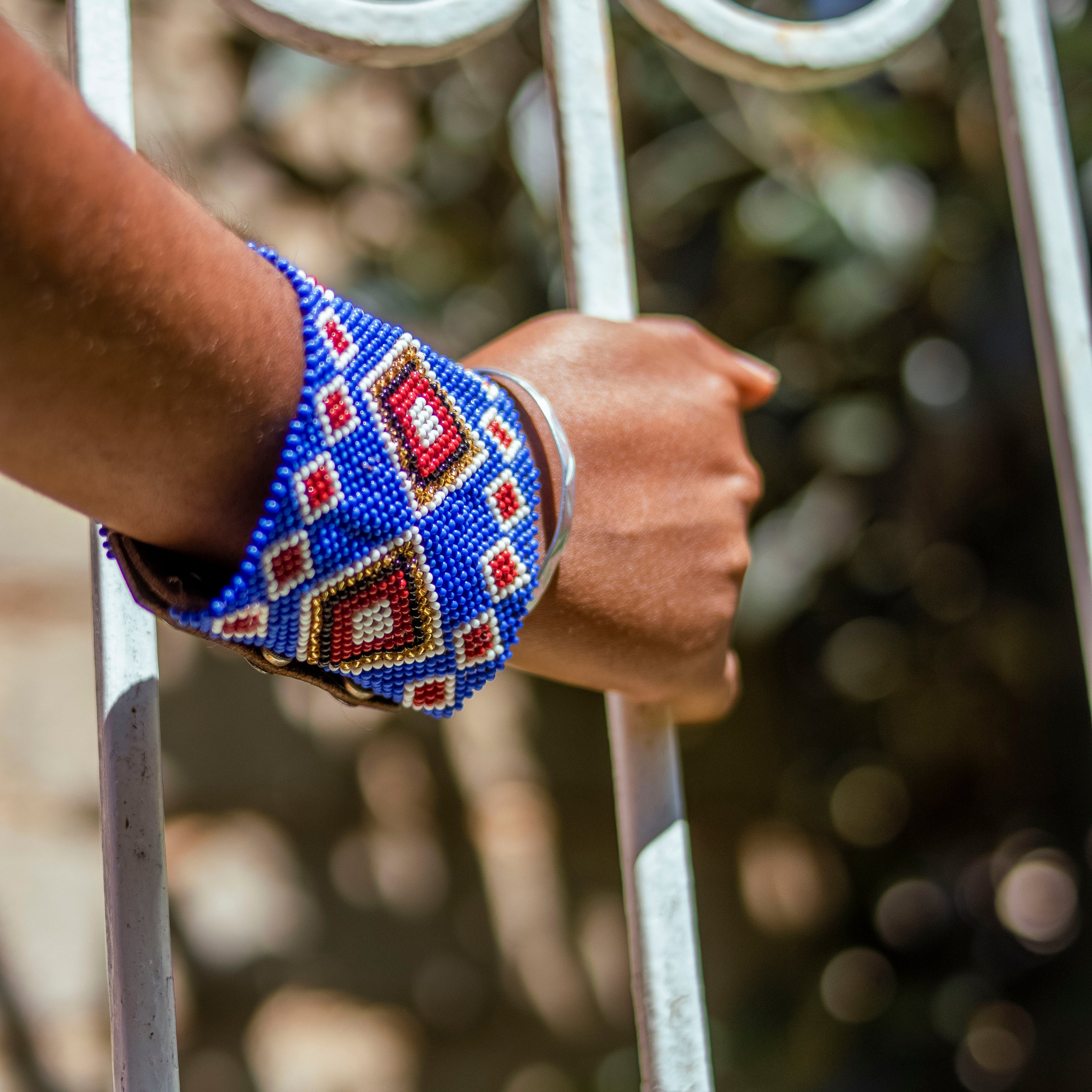 Hand wearing a colorful beaded bracelet on a metal gate.