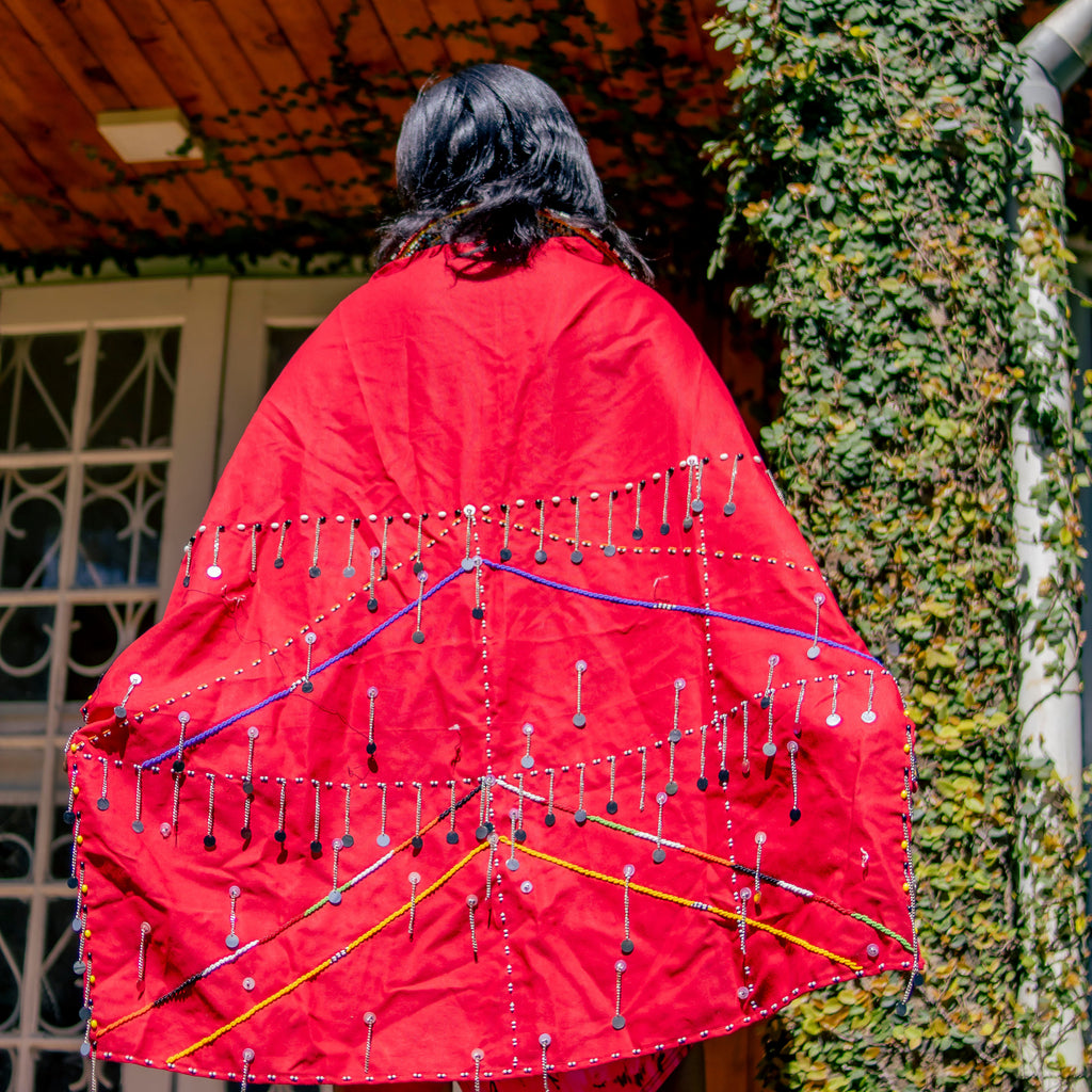 Person wearing a red garment with colorful patterns standing in front of a building with ivy.