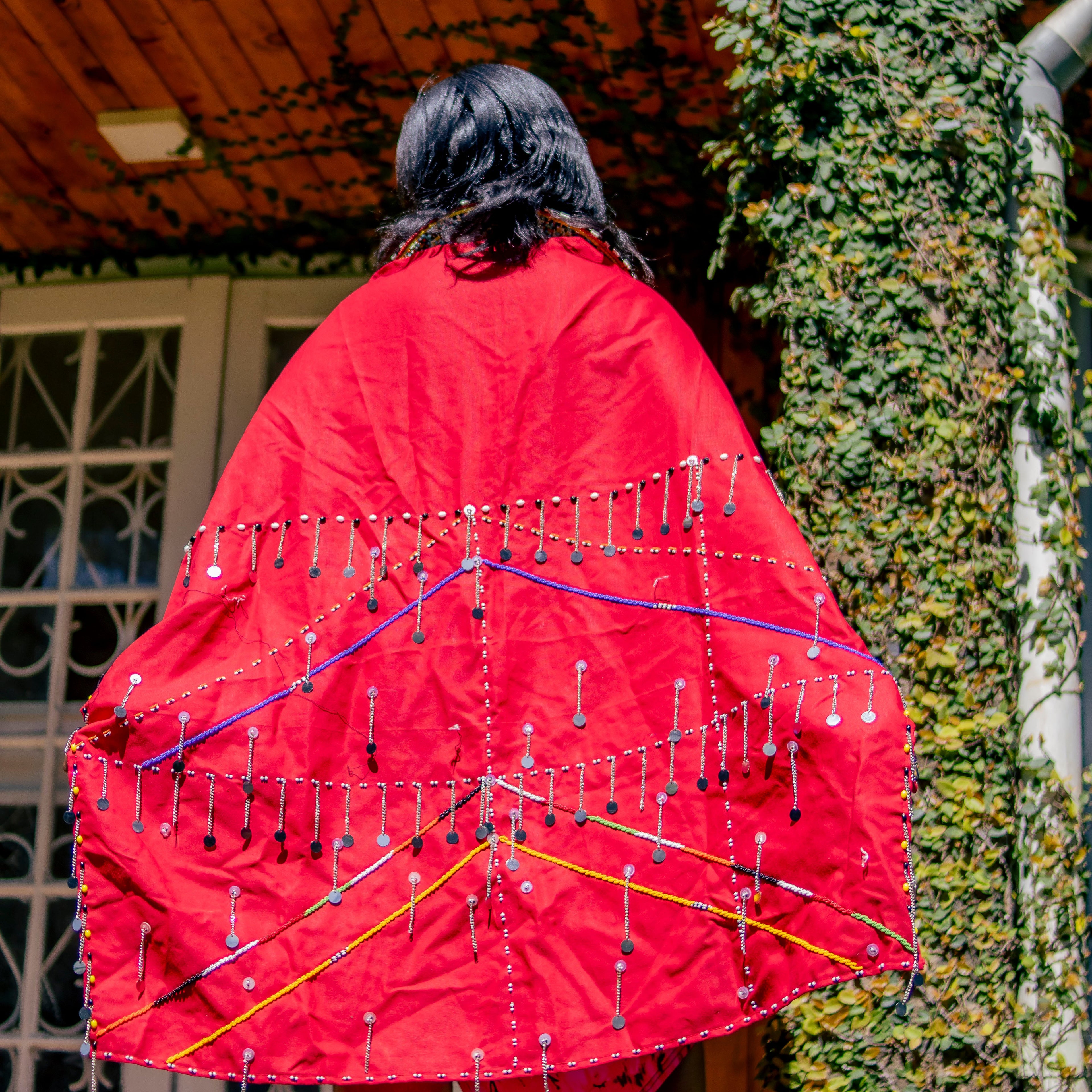 Person wearing a red garment with colorful patterns standing in front of a building with ivy.