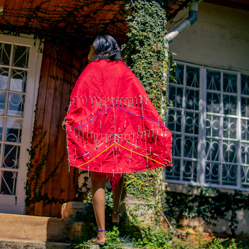 Person wearing a red garment walking up steps in front of a house with greenery.