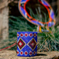 Blue beaded bracelet with geometric pattern on a stone surface, with blurred colorful maasai necklace in the background.