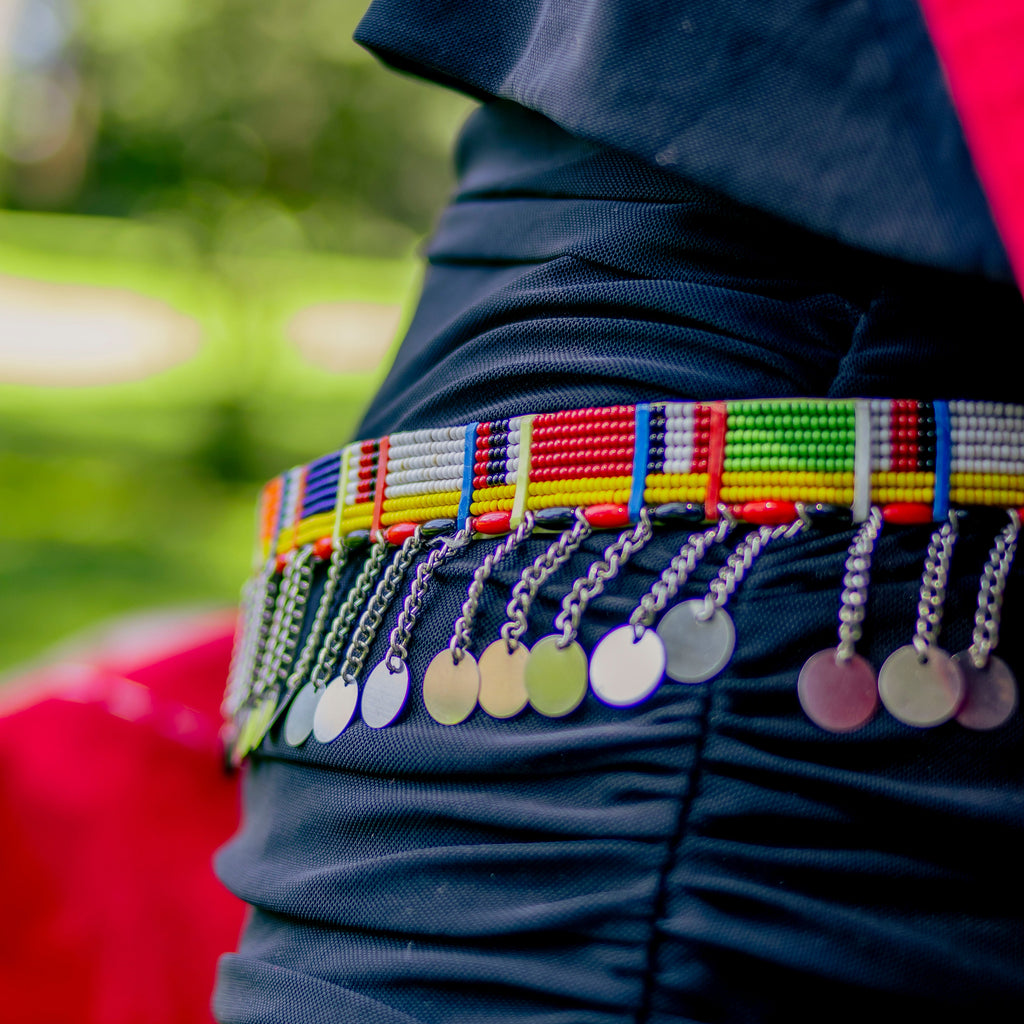 Colorful beaded belt with coins on a person wearing a dark outfit against a blurred natural background