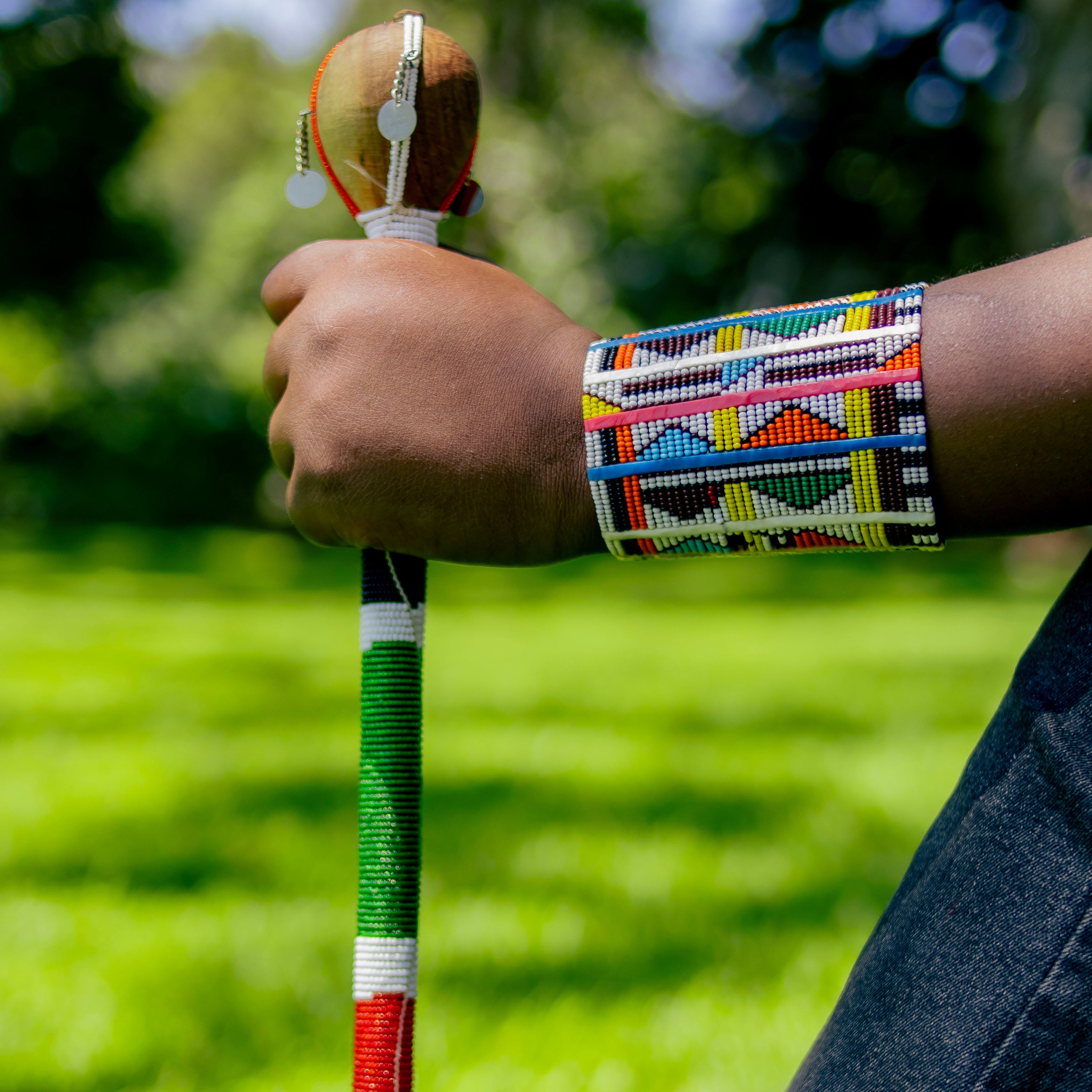 Person holding a decorated staff with a blurred green outdoor background
