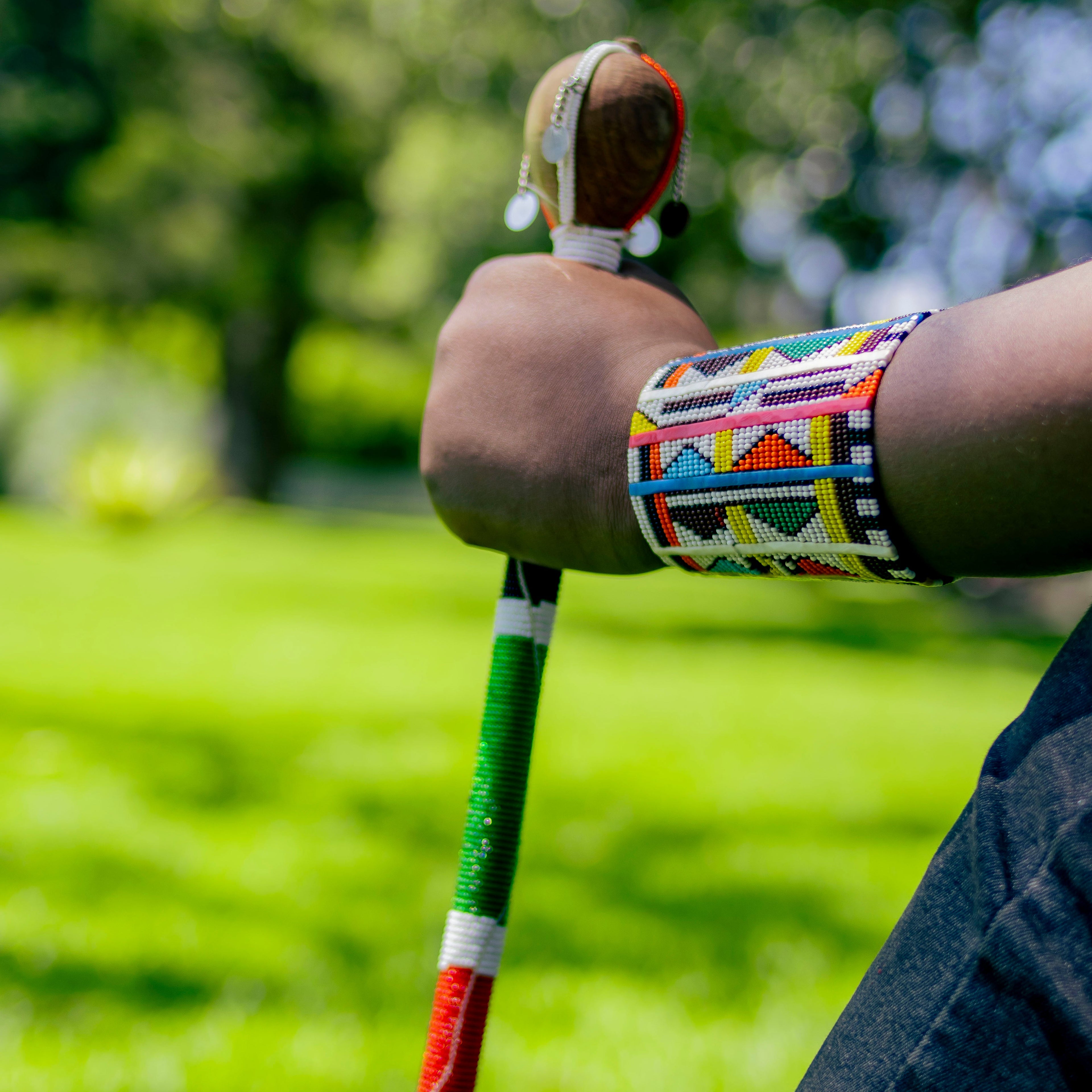 Person holding a colorful staff with a blurred green outdoor background