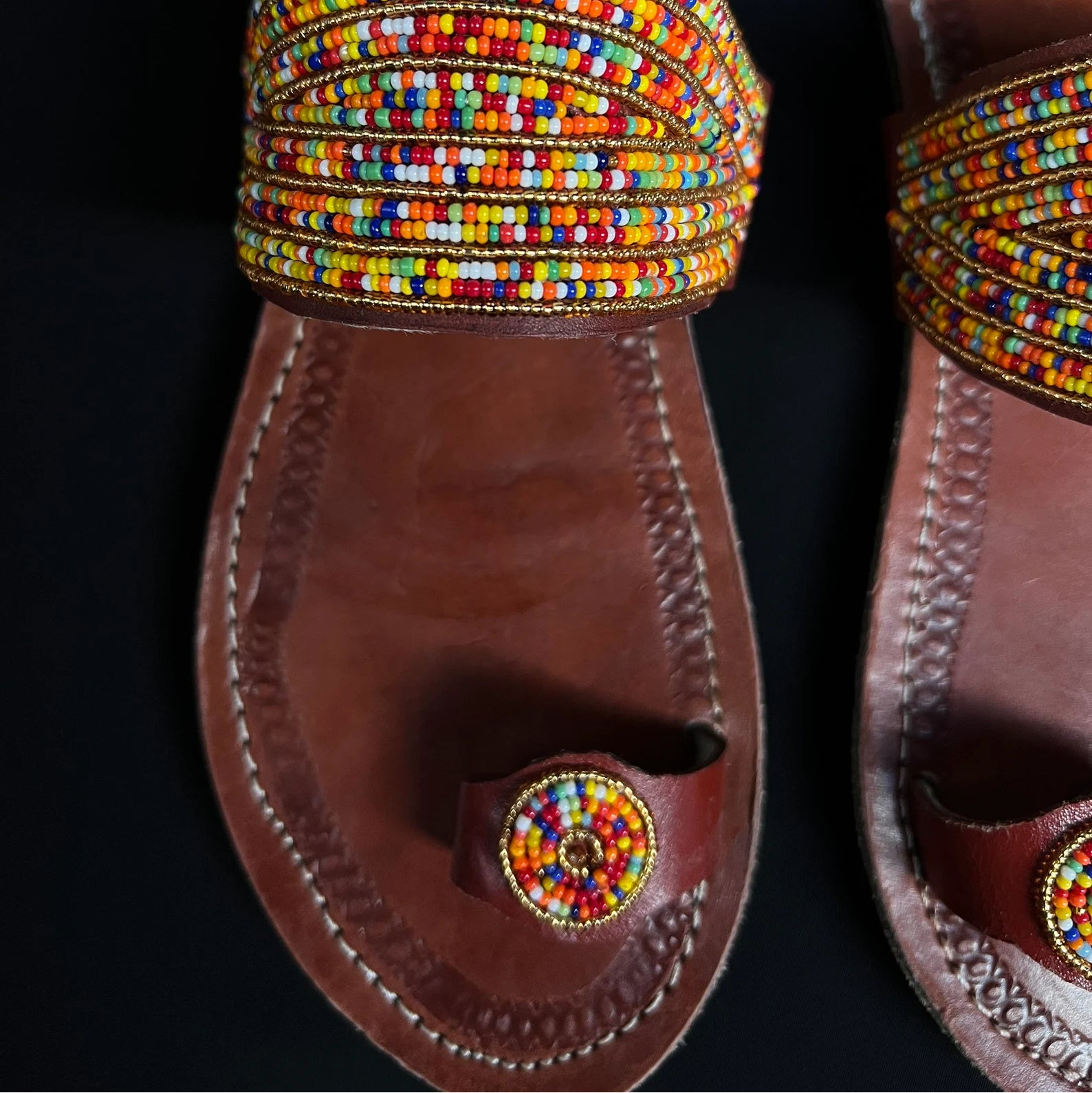 Pair of sandals with colorful beaded straps on a black background